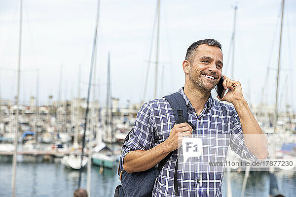 Smiling mature man talking on smart phone at harbor
