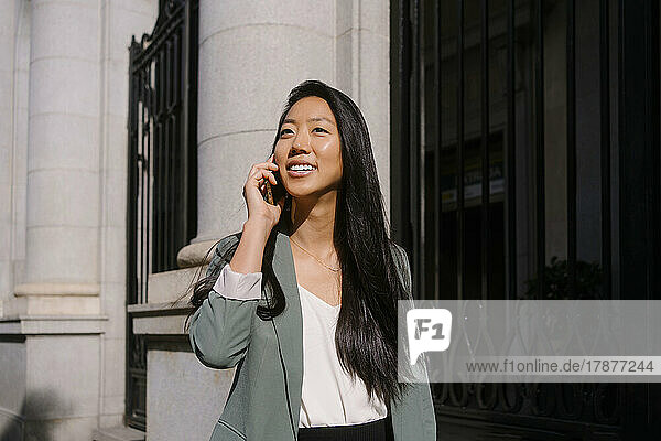 Young woman talking on smart phone in front of building