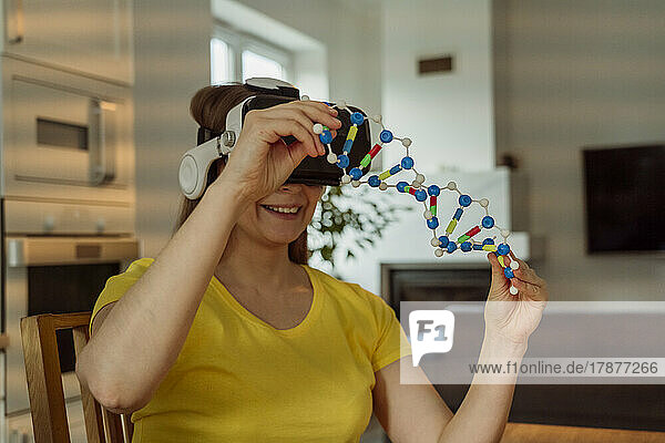 Lächelnde Frau mit VR-Brille und DNA-Modell zu Hause