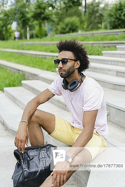 Man wearing sunglasses sitting with backpack on steps