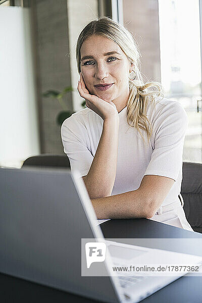 Blond businesswoman leaning on elbow sitting at desk in office