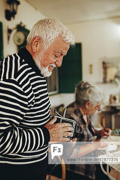 Senior man examining camera by woman painting at home