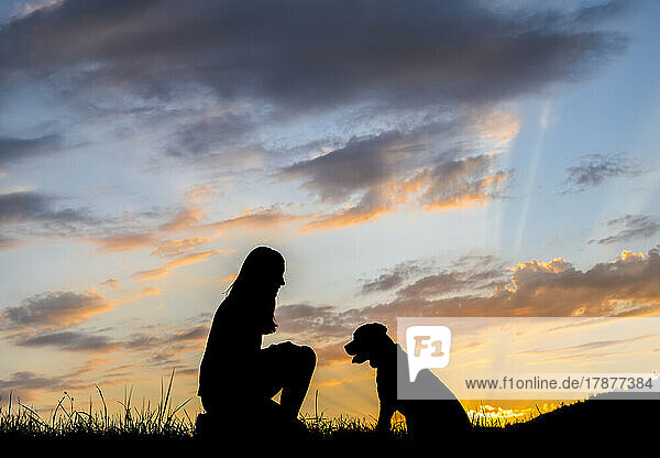 Silhouette einer Frau  die bei Sonnenuntergang mit Hund gegen Wolken spielt