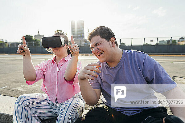 Brother laughing by sister with down syndrome wearing virtual reality simulator