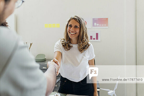 Lächelnde Geschäftsfrau schüttelt einem Kollegen im Büro die Hand