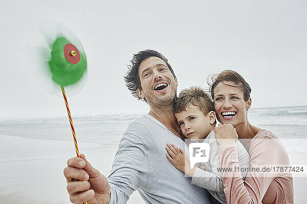 Glückliche Familie steht am windigen Strand und hält ein grünes Oinwheel in der Hand