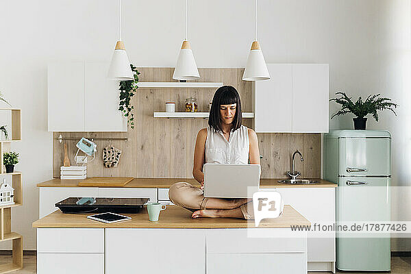 Freelancer using laptop sitting on kitchen island at home