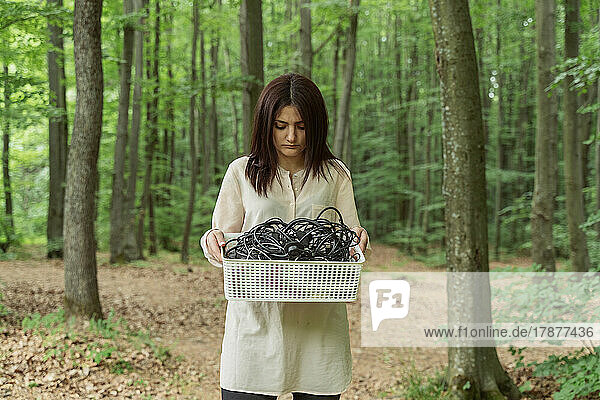 Frau steht mit einem Kabelkasten im Wald