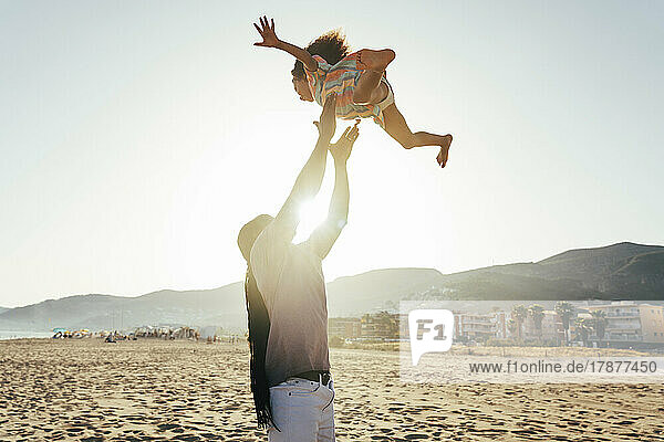 Playful father throwing daughter in air at beach