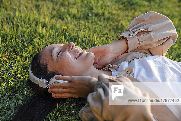 Smiling woman listening music through wireless headphones at park