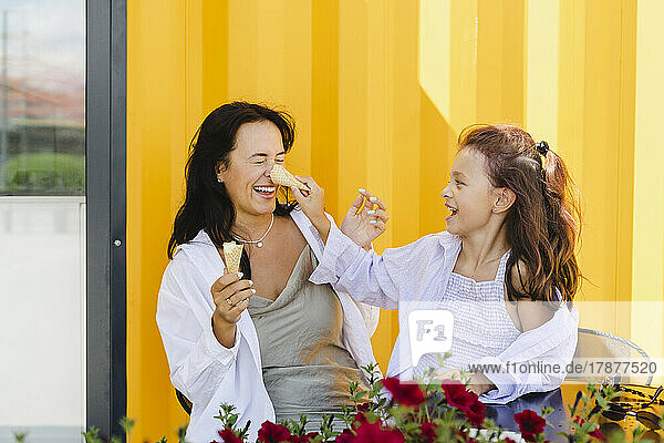 Cheerful mother and daughter with ice cream cone enjoying in front of yellow wall