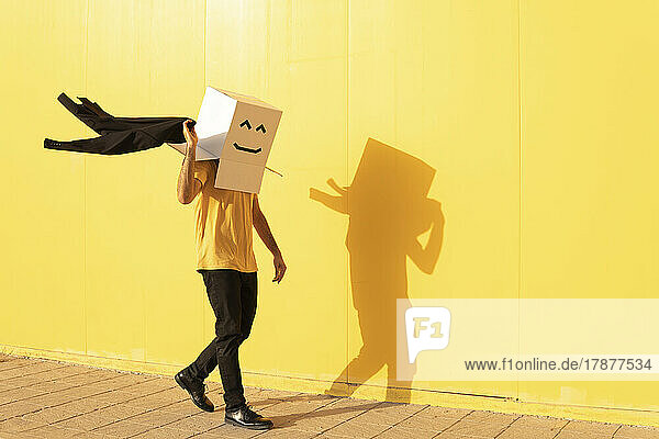 Man wearing box with smiley face holding jacket walking on footpath