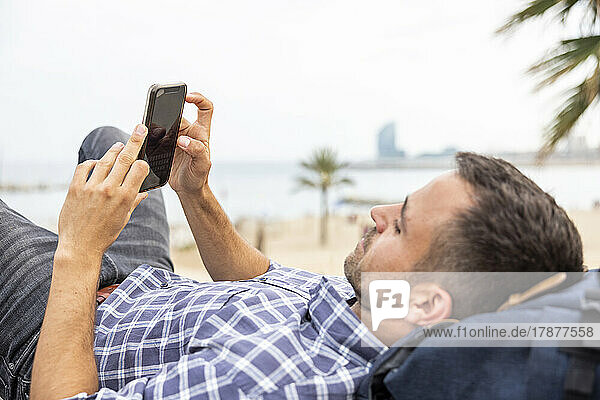 Mature man with mobile phone relaxing at beach