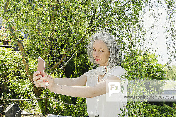 Smiling woman taking selfie through smart phone in park