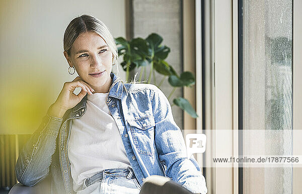Young businesswoman wearing denim jacket sitting in office on sunny day