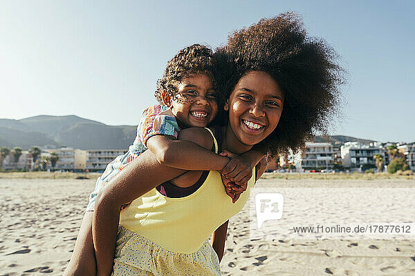 Happy girl piggybacking sister at beach
