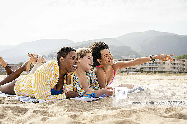 Woman pointing lying down with friends at beach