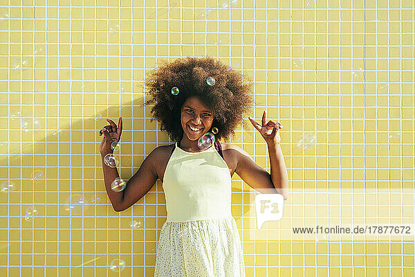 Fröhliches Mädchen mit Afro-Frisur  das ein Friedenszeichen zeigt