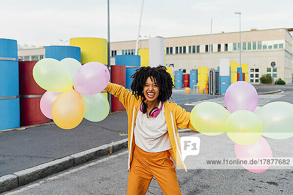Happy woman holding colorful balloons on footpath