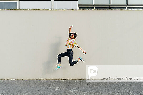 Cheerful woman jumping in front of wall