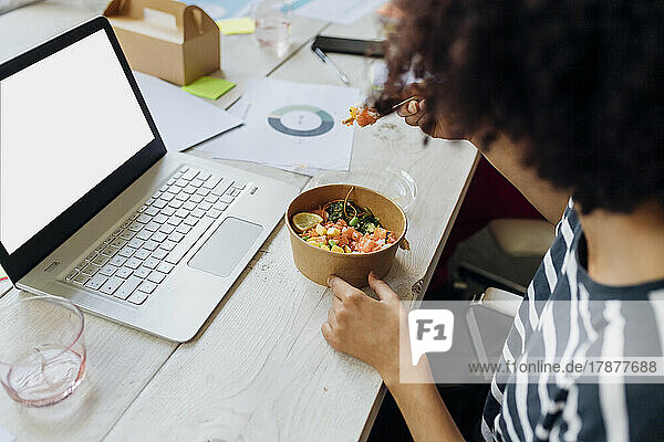 Businesswoman having poke bowl by laptop in lunch break at office