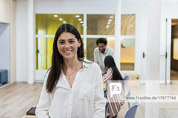 Portrait of smiling businesswoman in office with colleagues in background