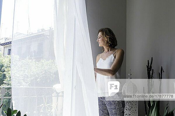 Mature woman looking out through window standing at home