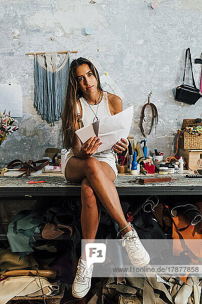 Fashion designer holding paper and tablet PC sitting on workbench