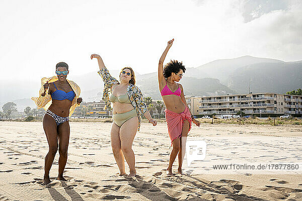 Carefree multiracial friends dancing at beach on sunny day