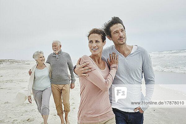 Adult couple walking with senior parents on the beach
