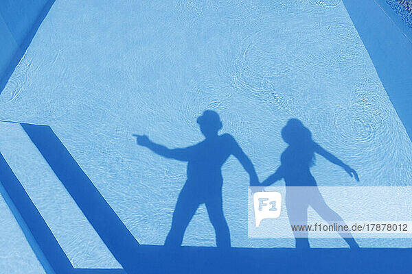 Shadow of man holding hand of woman seen on water of pool
