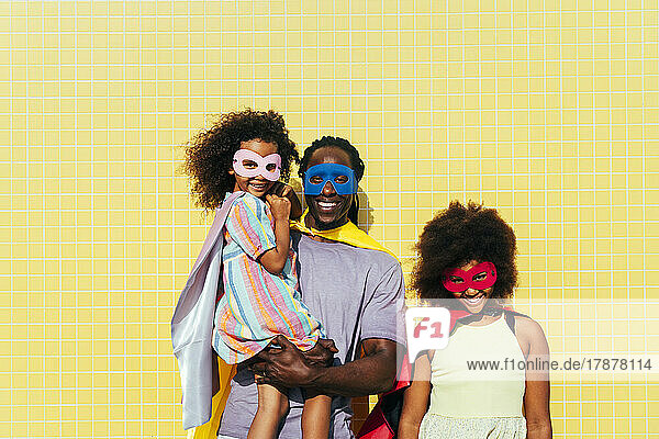 Lächelnder Vater mit Töchtern  die an einem sonnigen Tag Masken und Umhänge tragen