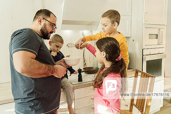 Father with children making omelet in kitchen