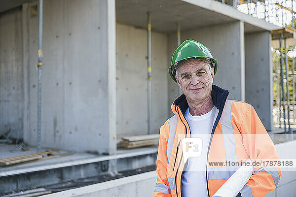 Lächelnder Bauunternehmer mit Bauplan steht auf der Baustelle