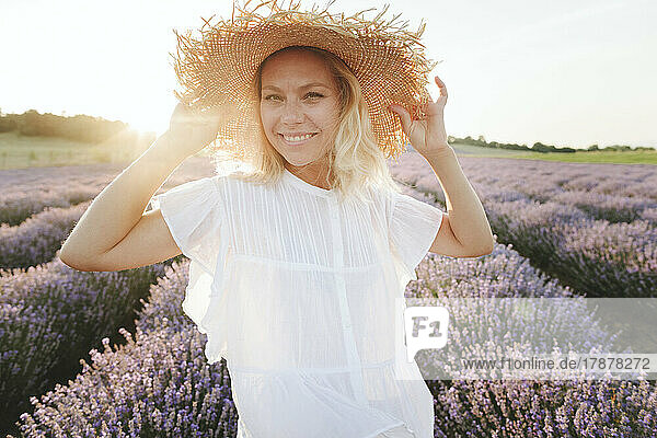 Smiling woman wearing straw hat standing in lavender field