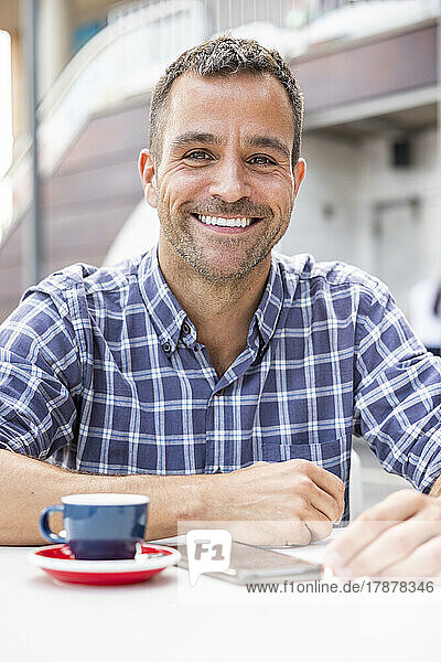 Happy mature man sitting with coffee cup at table at outdoor cafe