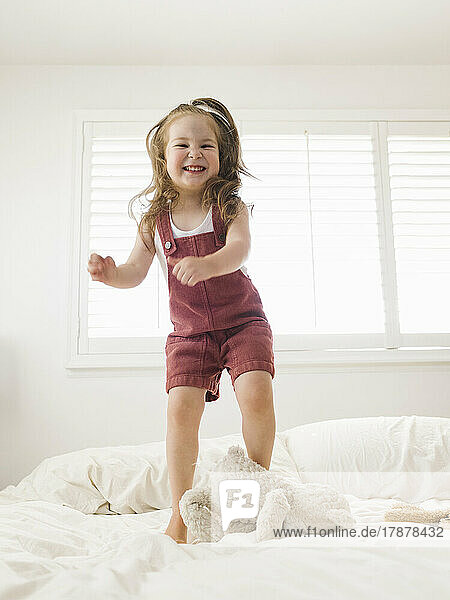 Smiling girl (2-3) jumping on bed