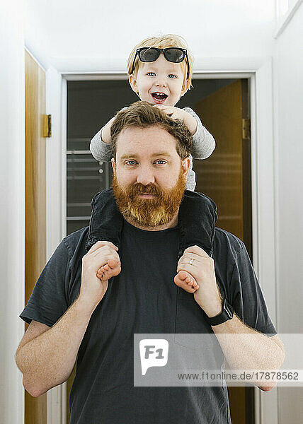Portrait of father carrying son (2-3) on shoulders at home