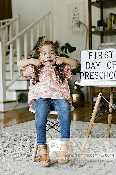 Portrait of girl (2-3) making faces at First day of preschool sign