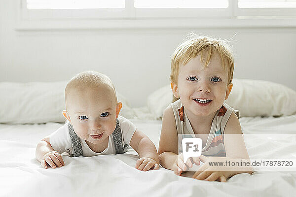 Portrait of brothers (6-11 months  2-3) lying on bed