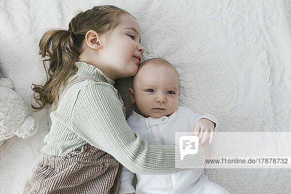 Girl (2-3) embracing newborn (0-1 months) brother on bed