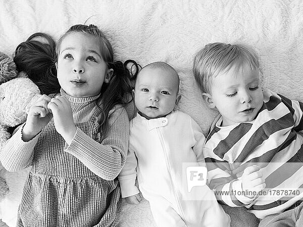 Brother and sister (2-3) with newborn boy (0-1 months) on bed