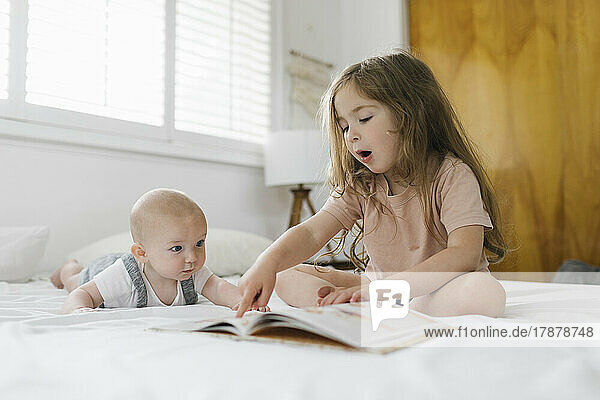 Girl (2-3) reading book to baby brother (6-11 months)