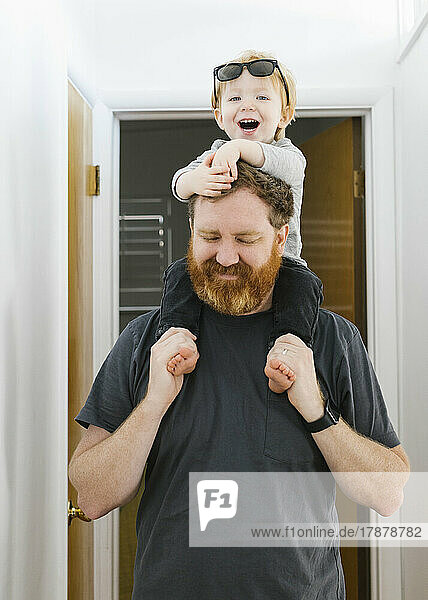 Father carrying son (2-3) on shoulders at home