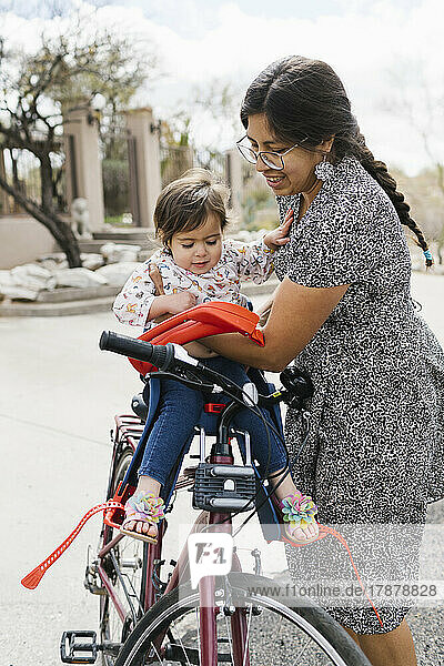 Mother placing daughter (2-3) in bike seat