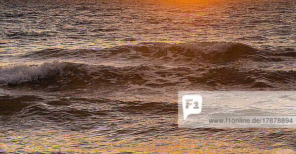 Close-up of ocean waves washing beach at sunrise