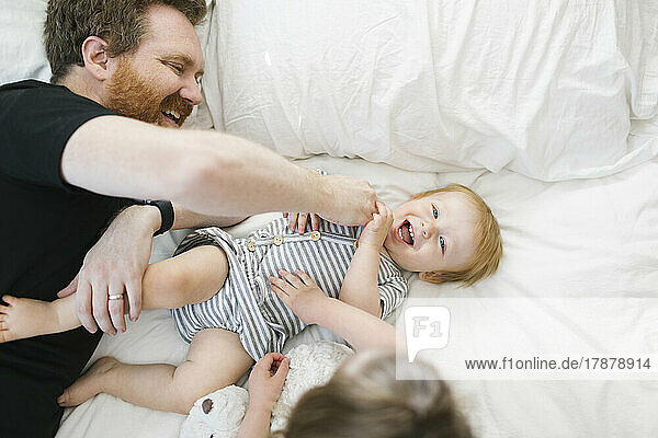 Father playing with son (12-17 months) and daughter (2-3) on bed