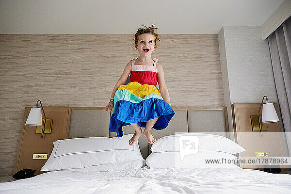 Smiling girl (4-5) jumping on bed
