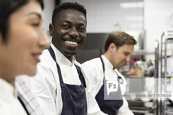 Porträt eines lächelnden Kochs inmitten von Kollegen  die in der Küche eines Restaurants arbeiten