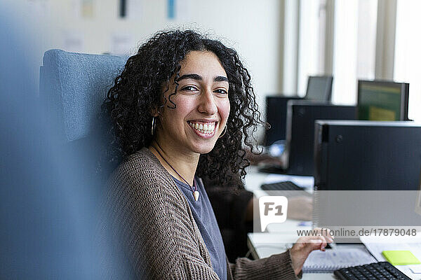 Seitenansicht einer glücklichen Geschäftsfrau  die am Schreibtisch im Büro sitzt